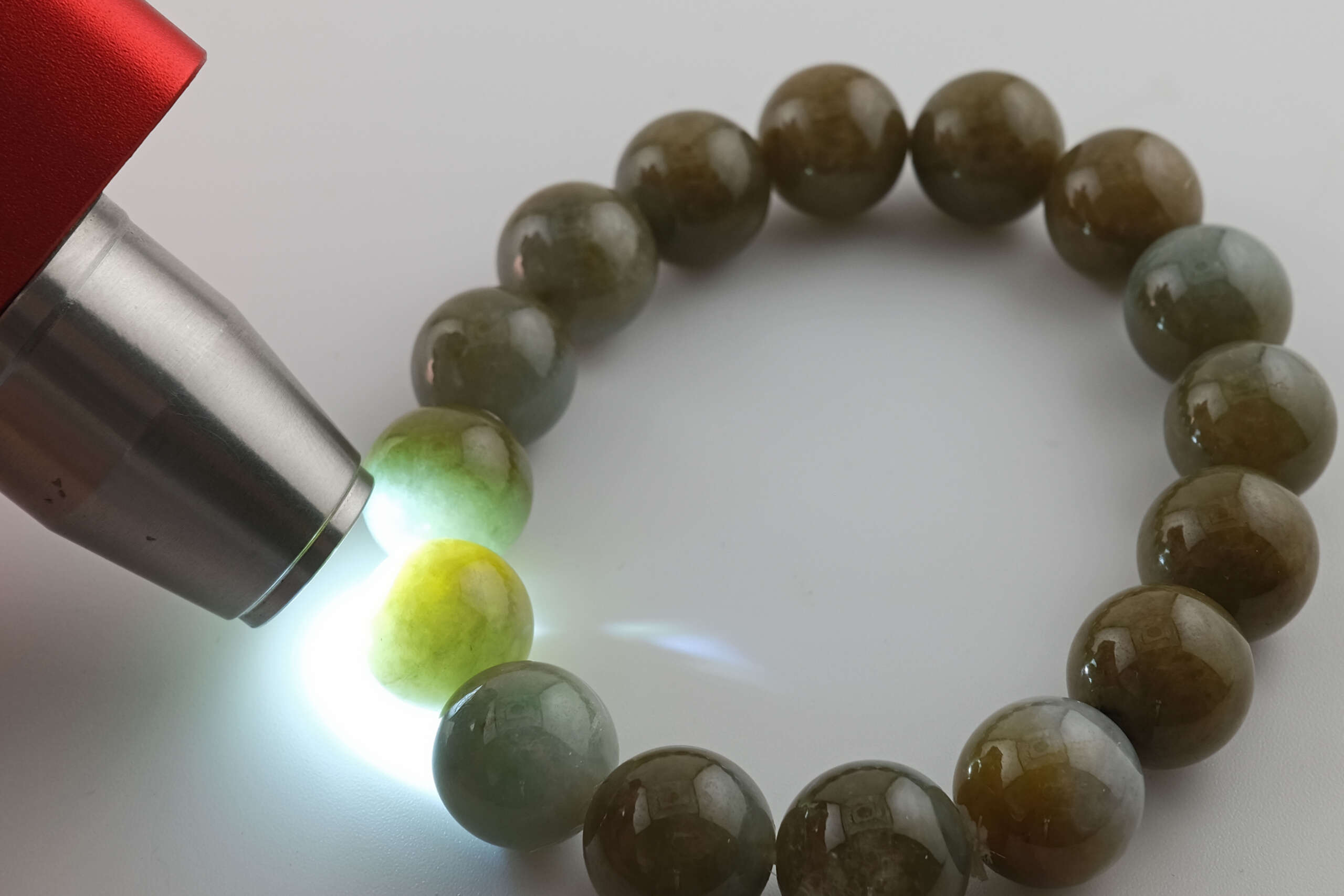 Close-up of natural Burmese A-type jadeite beaded bracelet under a jade light, showing semi-translucent green tone and internal texture revealed by strong illumination.
