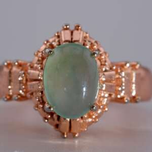 “Close-up of oval jadeite jade cabochon in icy light bluish-green color with reflective surface and rose-gold prong setting