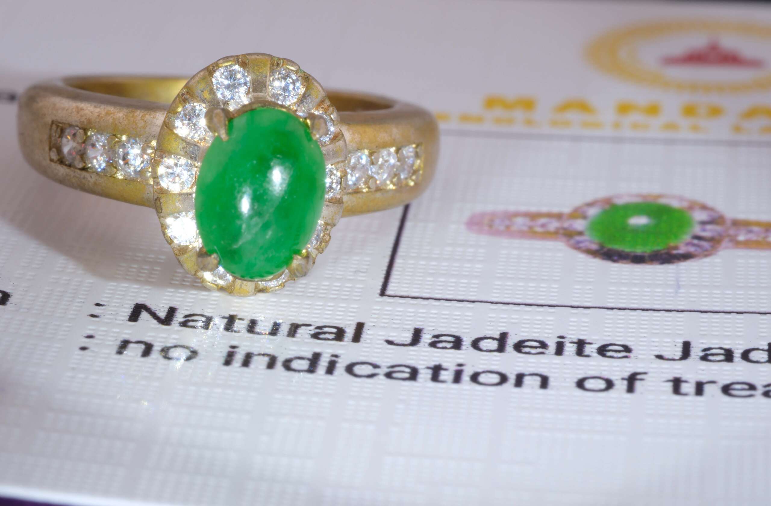Jadeite jade halo ring displayed on gem certificate, showing vivid green cabochon and gold-tone setting, size 5