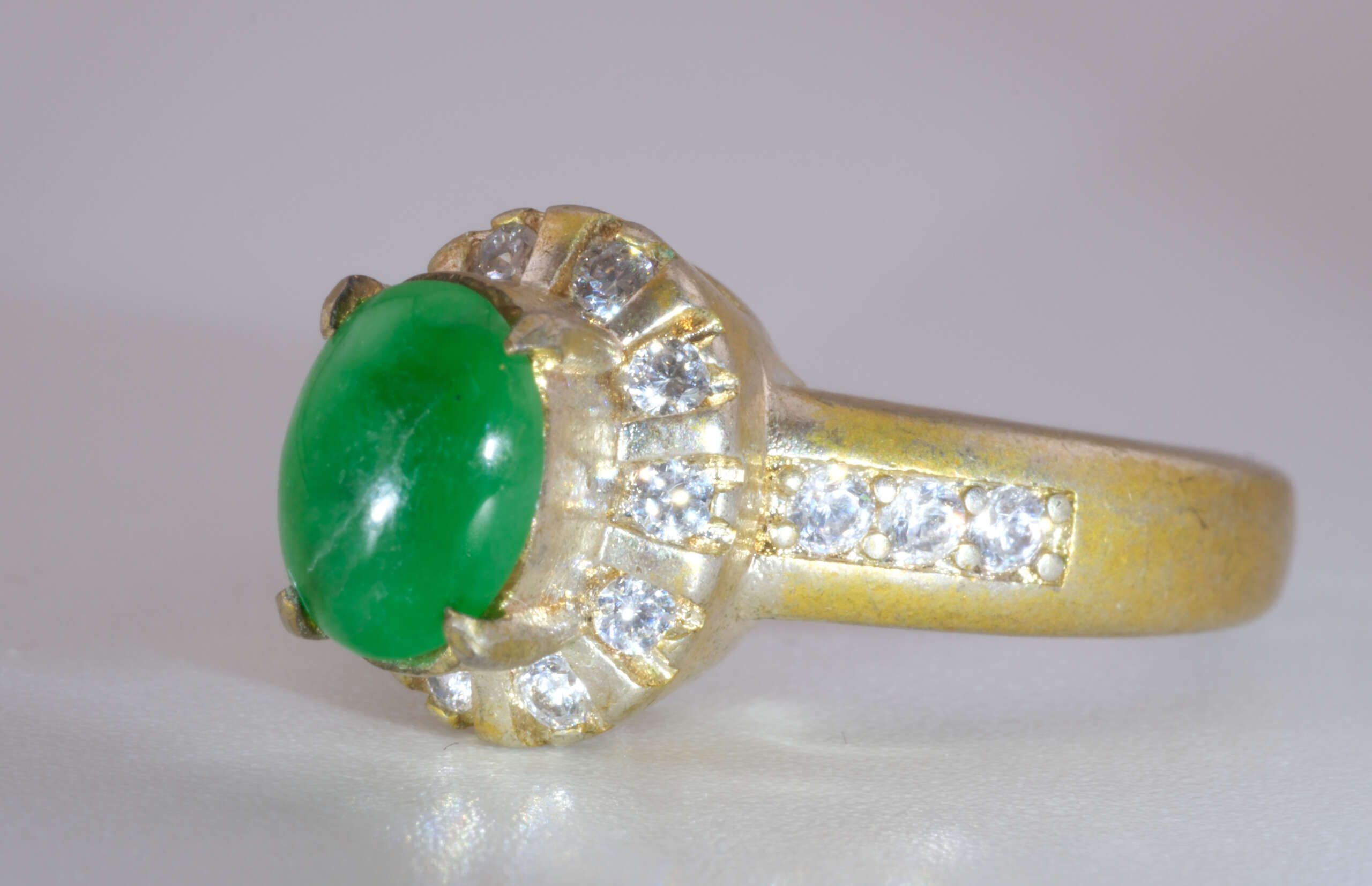 “Three-quarter photo of vivid green oval jadeite ring with white accent stones and matte gold band, size 5