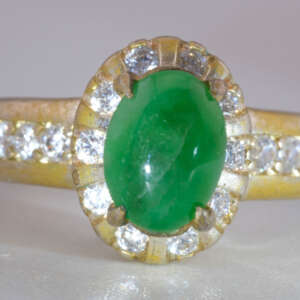 Front view of Type-A jadeite jade cabochon ring with halo of round accent stones and gold finish band, size 5