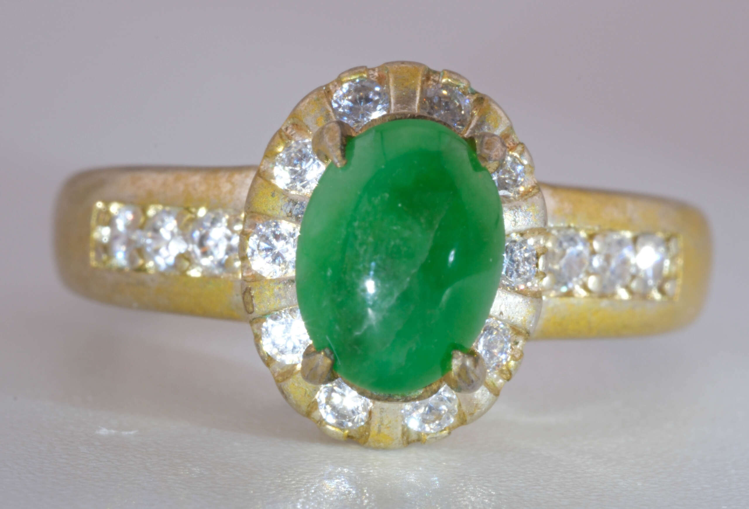 Front view of Type-A jadeite jade cabochon ring with halo of round accent stones and gold finish band, size 5