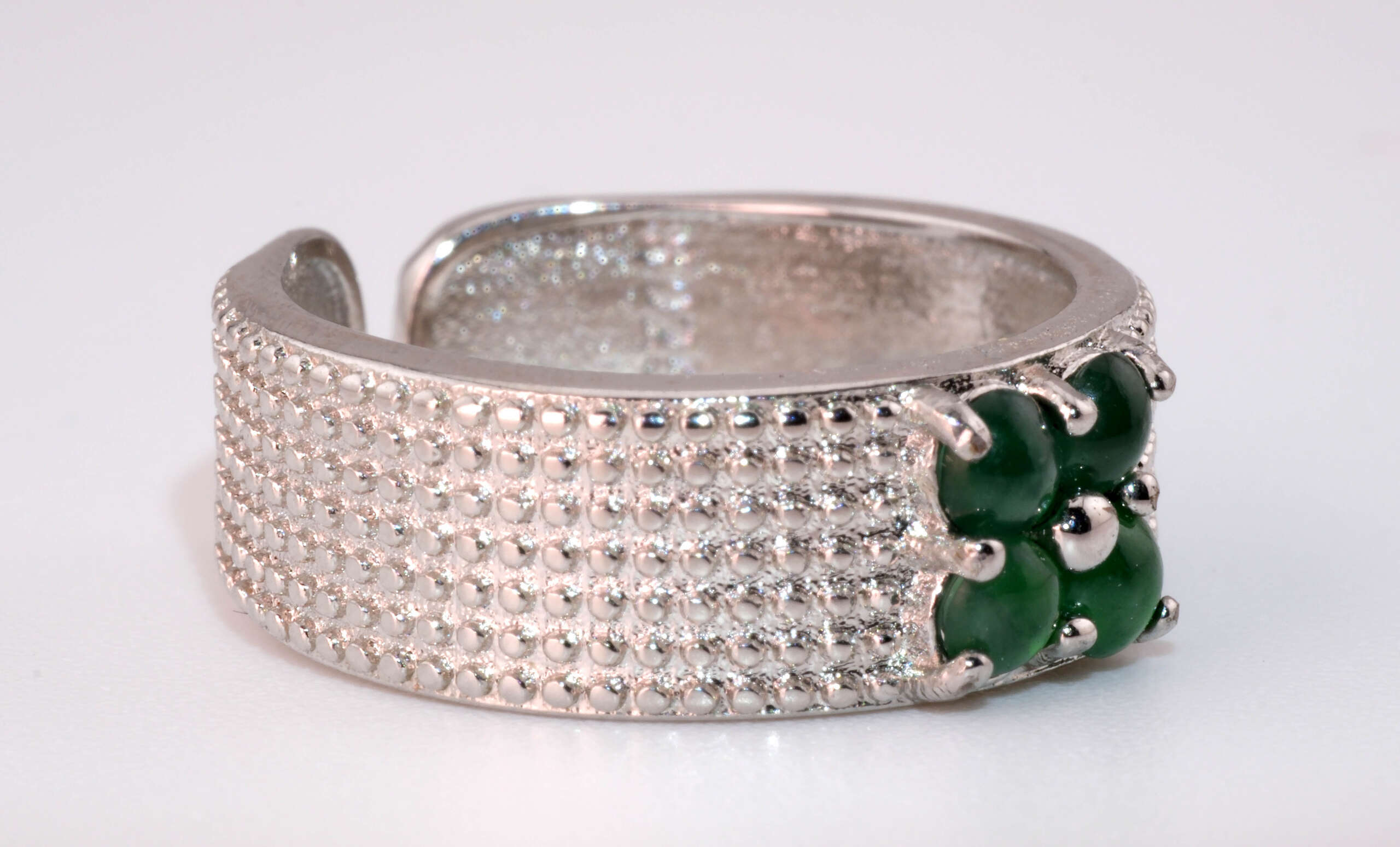 Angled shot of the jadeite cabochon cluster showing the wide silver textured band and prong settings.