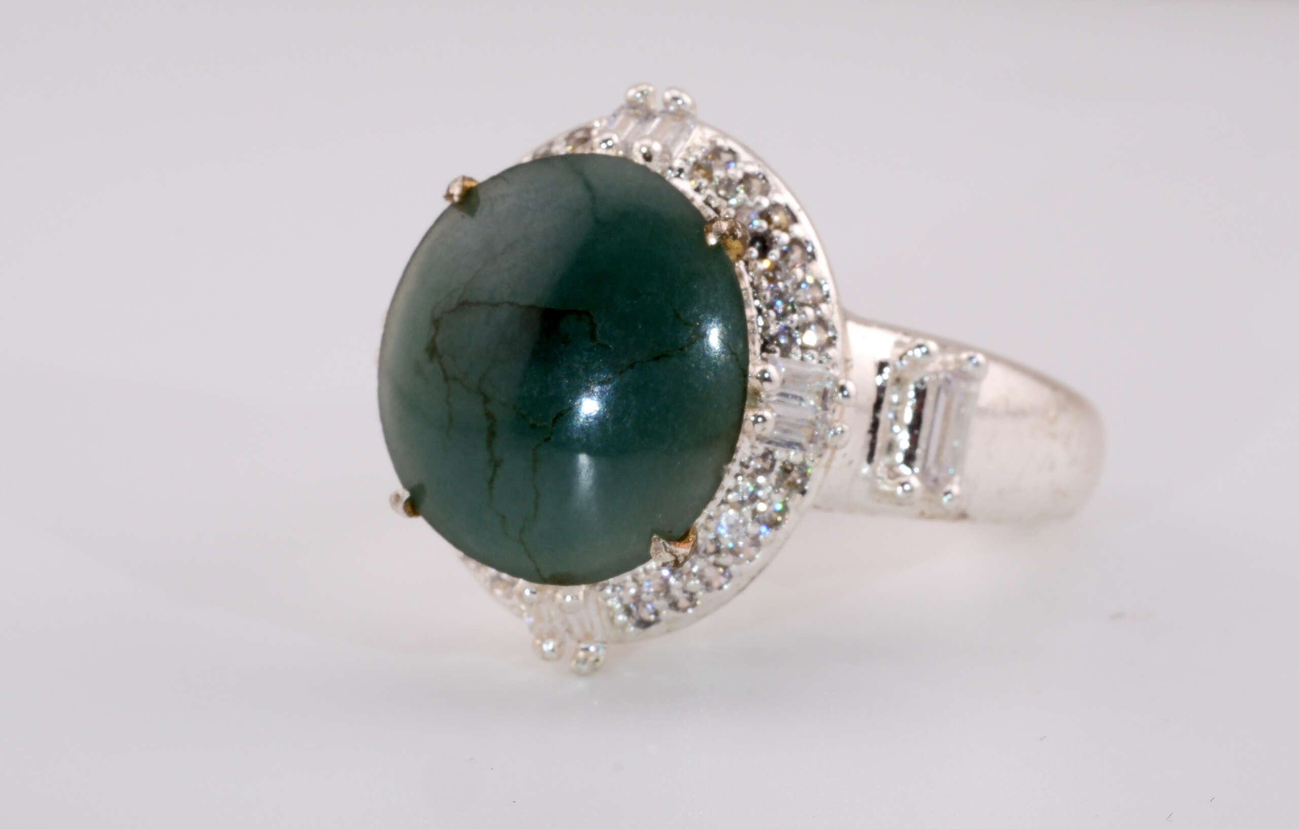 Close-up side view of the jadeite ring showing the bluish-green cabochon and sparkling halo of round and baguette stones set in silver