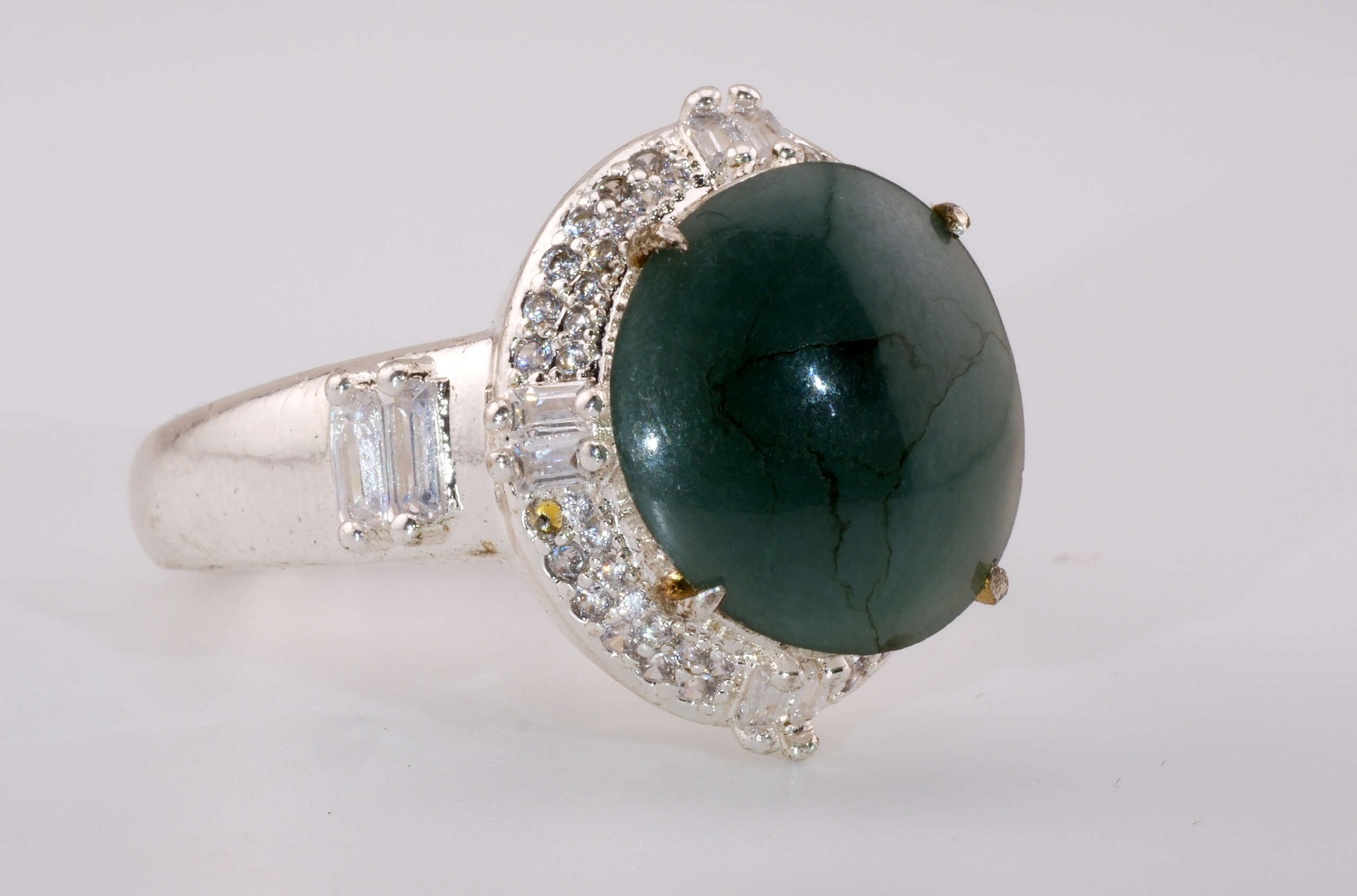 Close-up side view of the jadeite ring showing the bluish-green cabochon and sparkling halo of round and baguette stones set in silver