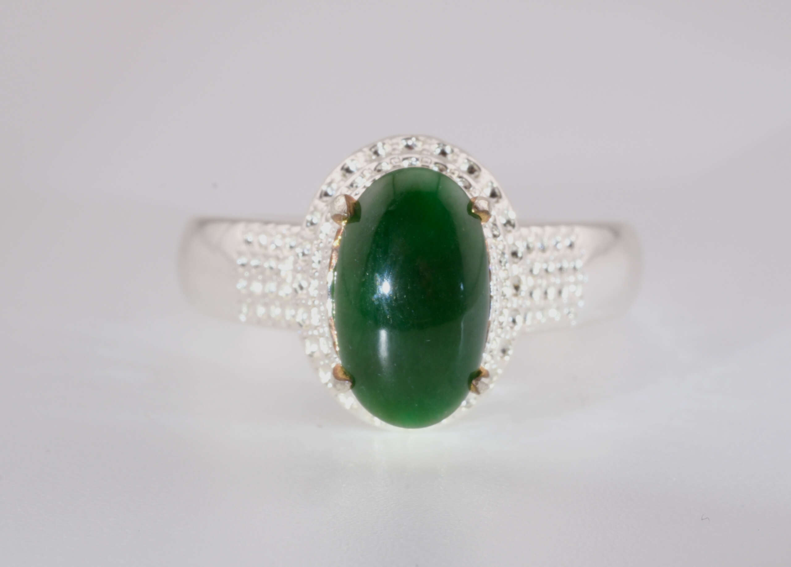 “Front-facing close-up of a natural green jadeite jade cabochon ring set in a silver mount with micro-pavé detailing
