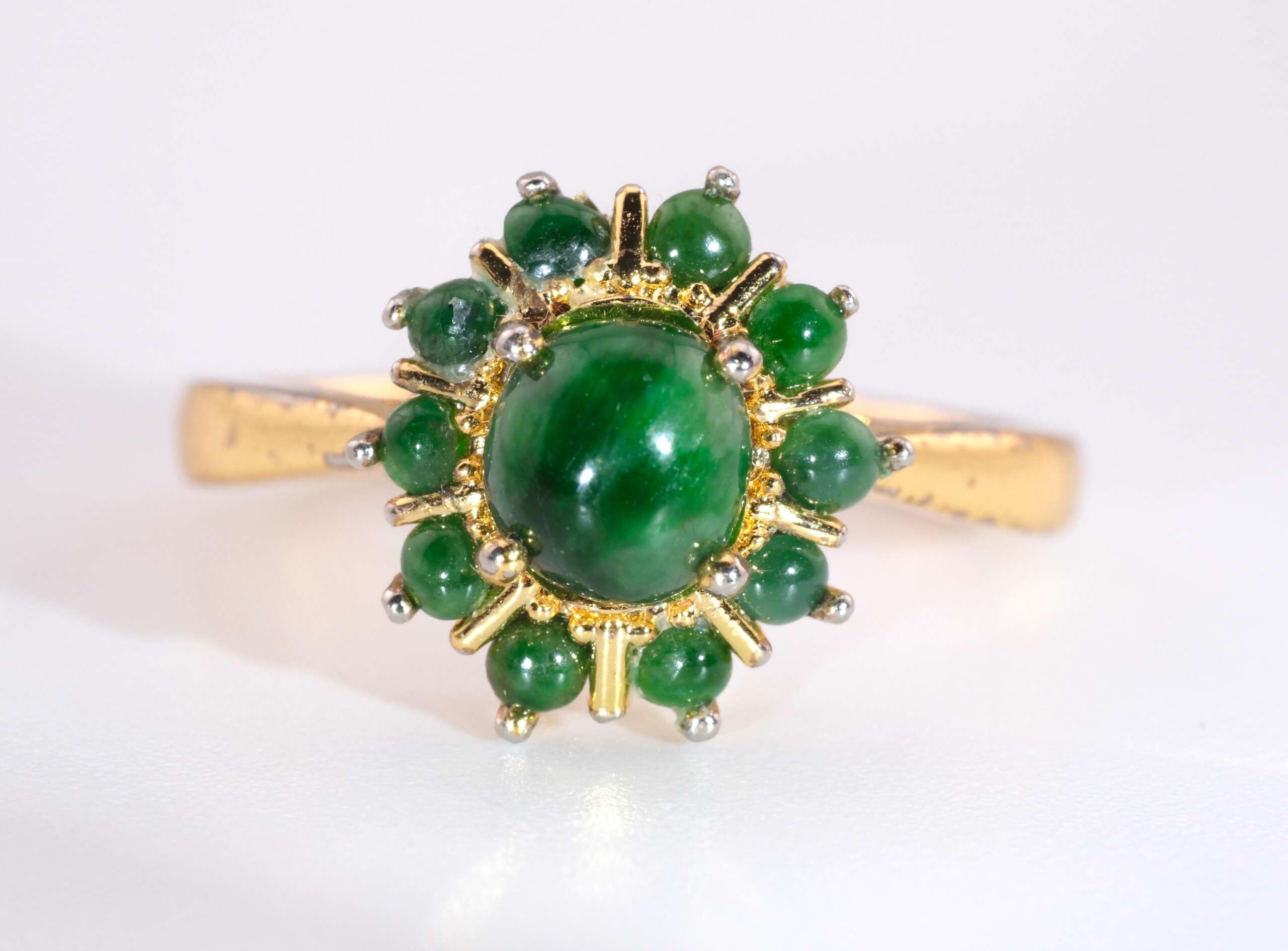 A gold-plated ring featuring a glossy green jadeite cabochon at the center, surrounded by a circular halo of small round jade cabs in a floral arrangement.