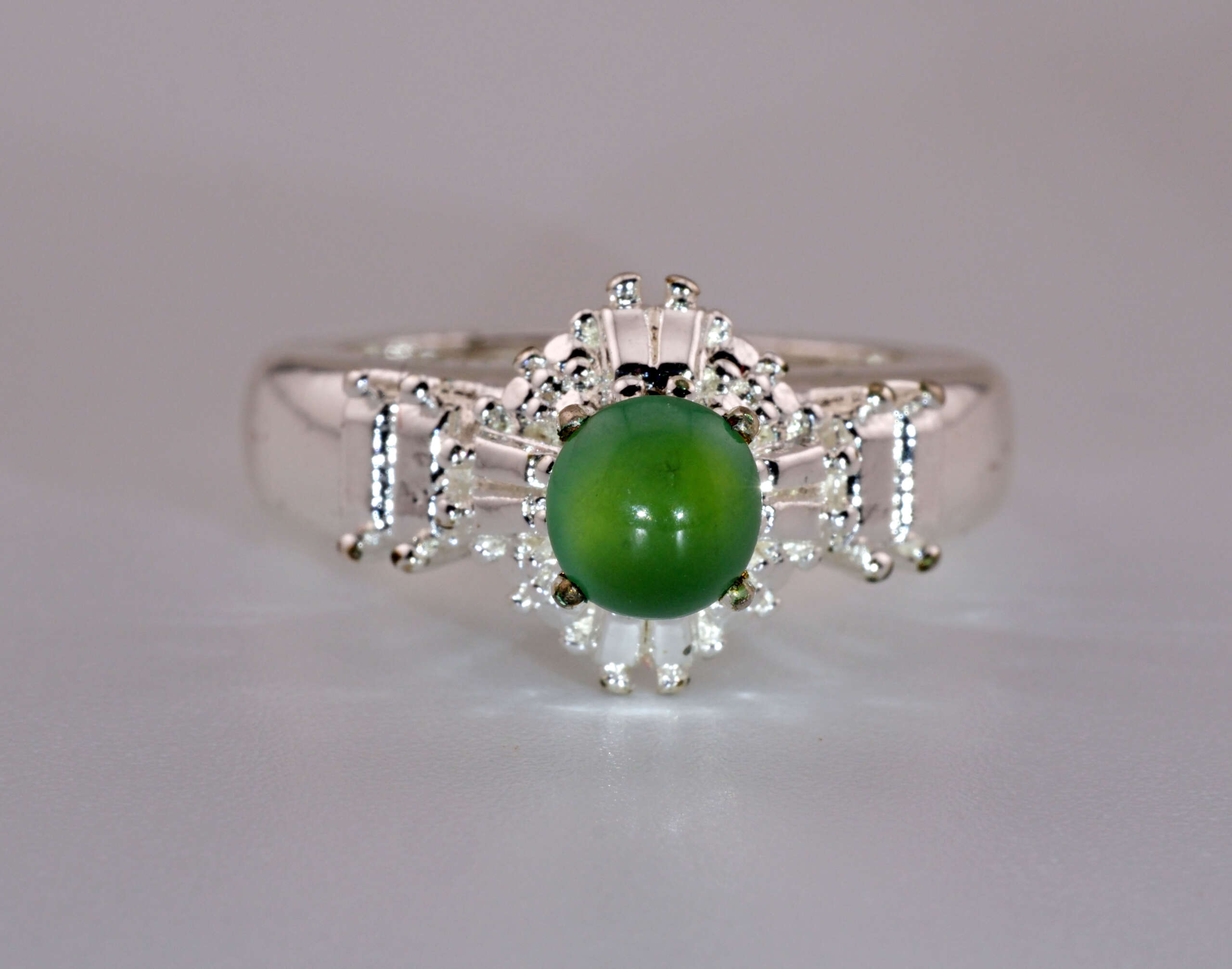 Front view of a natural green jadeite cabochon ring, highlighting the smooth round cabochon and decorative silver setting
