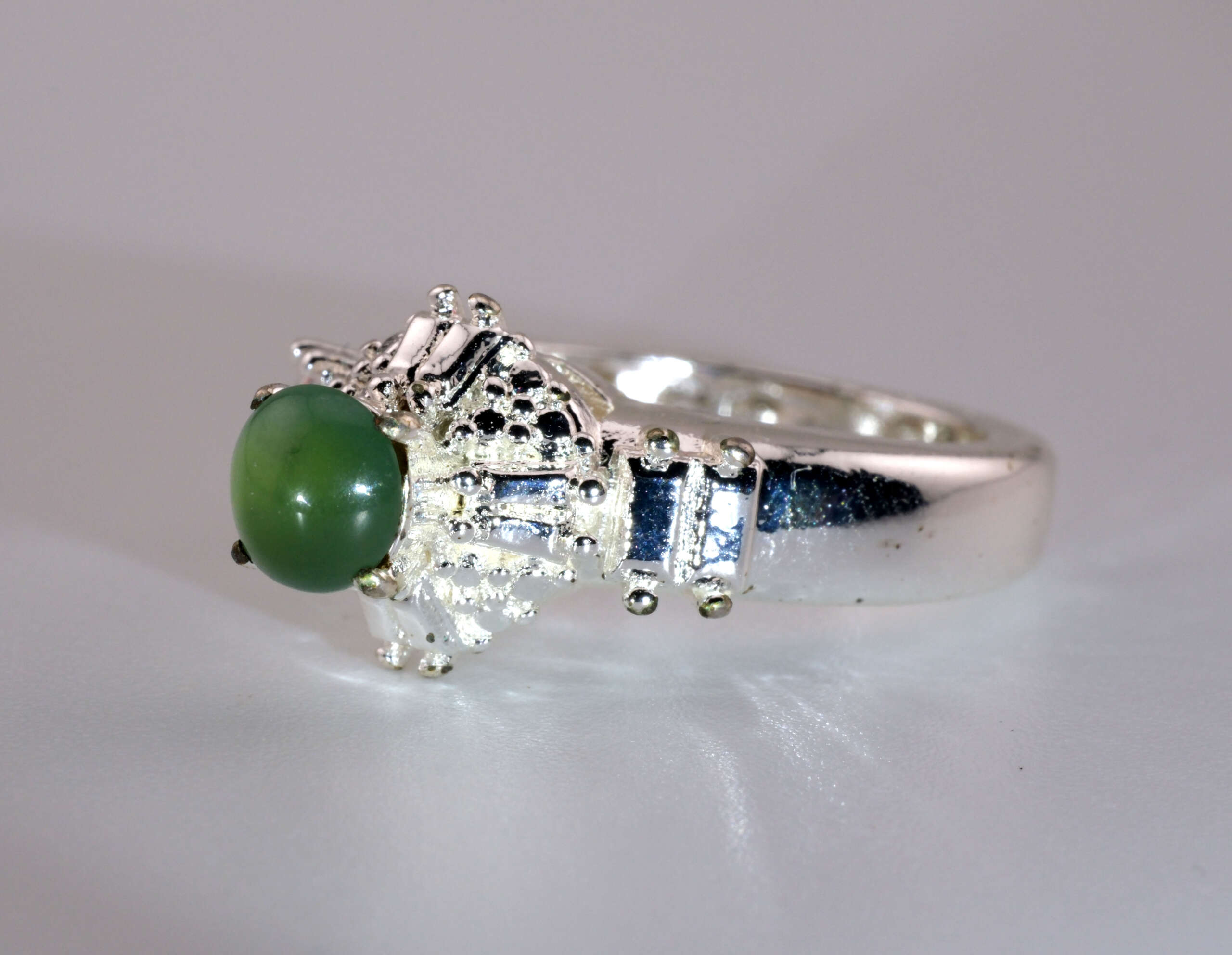 Side view of the jadeite ring showing bright green cabochon and silver accent bars on the shoulders.