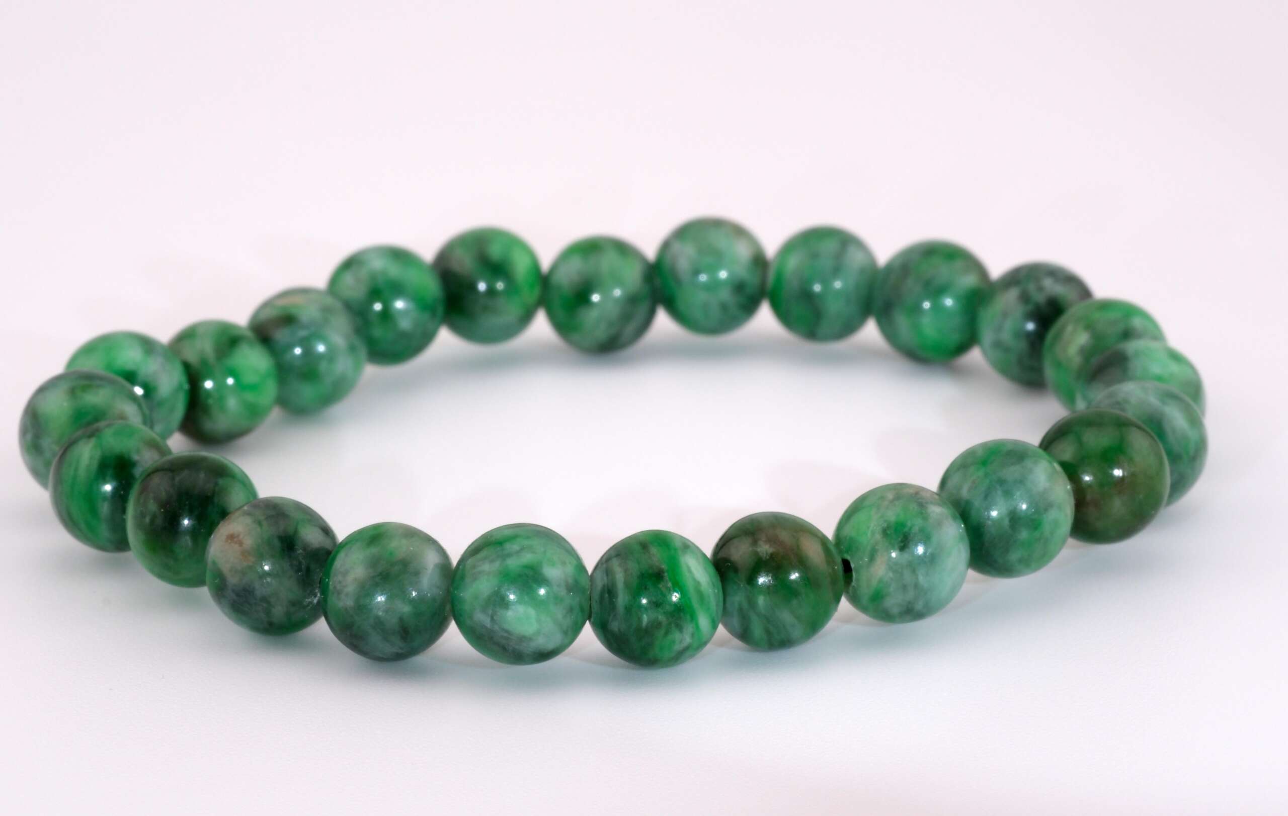 A stretch bracelet composed of uniformly sized green Maw Sit Sit beads on a white surface, showing the mix of emerald, forest, and mint-green patterns.