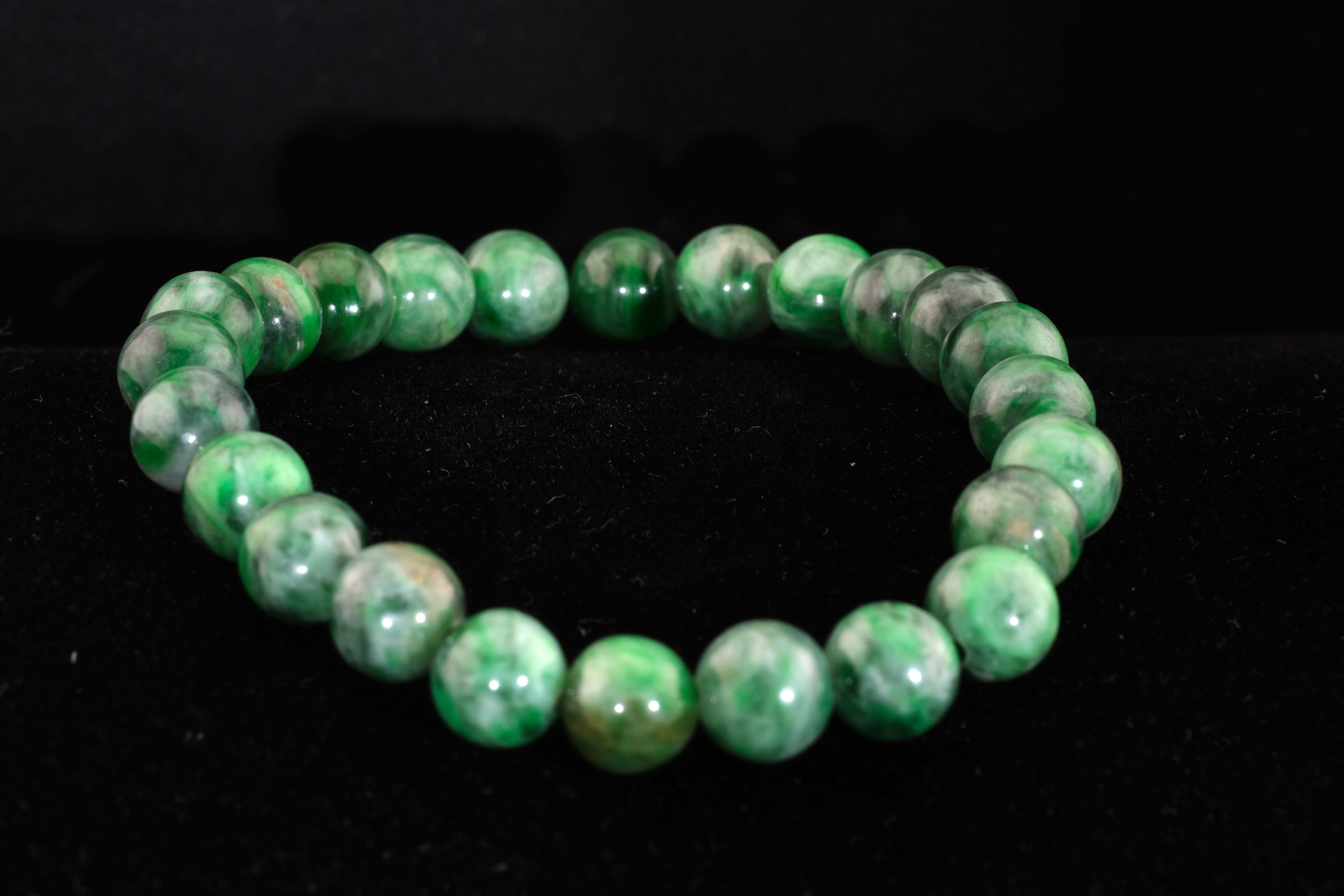 Close-up view of a Maw Sit Sit jadeite bracelet on a black background, highlighting the stone’s deep chromian greens and marbled texture