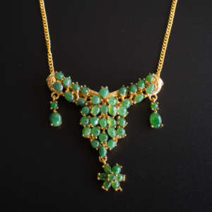 Gold-tone alloy necklace with clustered green jade cabochons, triangular pendant and floral drop, photographed on black background.