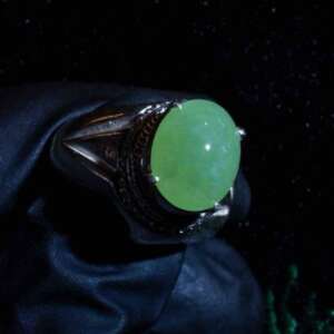 Angled side view of natural jadeite cabochon ring highlighting green polish and mixed alloy mounting.
